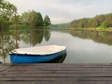 Fototapeta  - Wooden boat on the pier on the background of the lake. Fishing boat on the shore of a forest reservoir. The boat is tied to the shore. Concept: outdoor recreation, tranquility by the water.