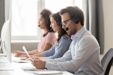 Wall Mural - serious call center agent in wireless headset holding, reading paper documents, sitting at workplace