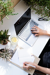 Woman's hands on laptop keyboard, writing in notepad