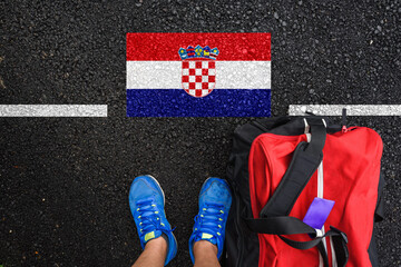 a man with a shoes and travel bag is standing on asphalt next to flag of Croatia  and border 