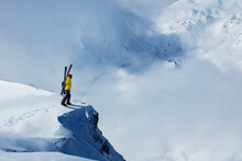 Adult man stand on the mountain top cliff with backpack and ski observe long alpine panorama to concur skiing