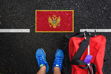 Wall Mural - a man with a shoes and travel bag is standing on asphalt next to flag of Montenegro  and border 