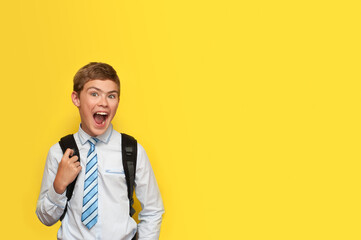 A boy in a shirt and tie with a school backpack emotionally rejoices, smiling on a yellow background.