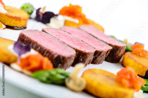 Closeup of roasted beef slices surrounded by vegetables and herbs isolated on a white background © Wirestock 