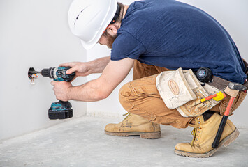 Electrician Builder at work, installation of lamps at height. Professional in overalls with a drill. On the background of the repair site.