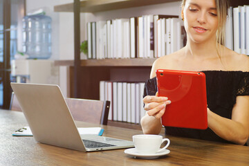 Beautiful young Caucasian woman sitting and using her tablet and computer searching for information online with cup of hot coffee. Working woman lifestyle at home or cafe concept