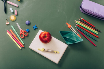 Wall Mural - top view of ripe apple and dividers on book near paper boat and school supplies on green chalkboard