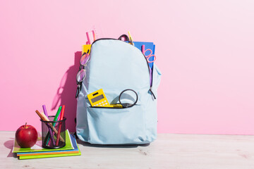 Wall Mural - School backpack full of stationery near copy books, apple and pen holder with felt pens on pink