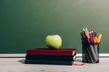 Wall Mural - Ripe apple on books near pen holder with school supplies on desk near green chalkboard