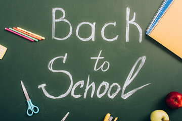 Wall Mural - top view of back to school lettering near apples and school supplies on green chalkboard