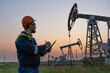 © Сергей Храмов - Oil worker checks an oil rig at sunset. Maintenance of oil pump jacks