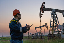 Oil Worker Checks An Oil Rig At Sunset. Maintenance Of Oil Pump Jacks