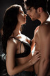 © LIGHTFIELD STUDIOS - Brunette woman in bra touching torso of sexy boyfriend on black background