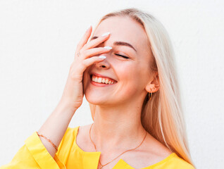 Vivacious woman giglling with her eyes screwed up in a moment of fun as she sitting against white studio wall. Happy natural laughing young casual female covering mouth. Human face expressions