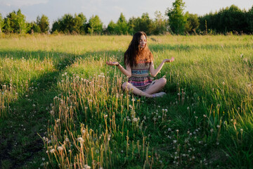 Young woman practicing yoga sitting in easy pose outdoors in green field. Unity with nature concept.