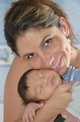 Mãe muito feliz e sorridente segurando seu bebe pequeno no colo 