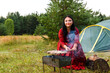 A young gypsy woman grills meat near the tent.