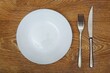 © Mari_Vik - Clean empty white round plate And cutlery metal fork and knife On a wooden table