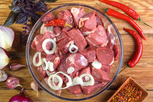 Boneless Lamb Steak, Sliced And Marinated With Onions, Meat In A Glass Bowl, Basil, Chili Peppers, Marinades On A Wooden Table, Top View, Close-up.