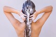 A naked woman shampooing her hair in the shower.