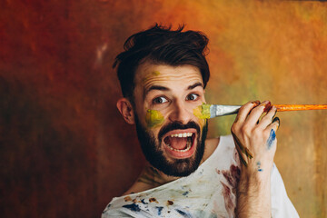 Portrait of a young creative artist, man wearing a white T-shirt with colored spots from paint posing for a photo in the process of creating a picture