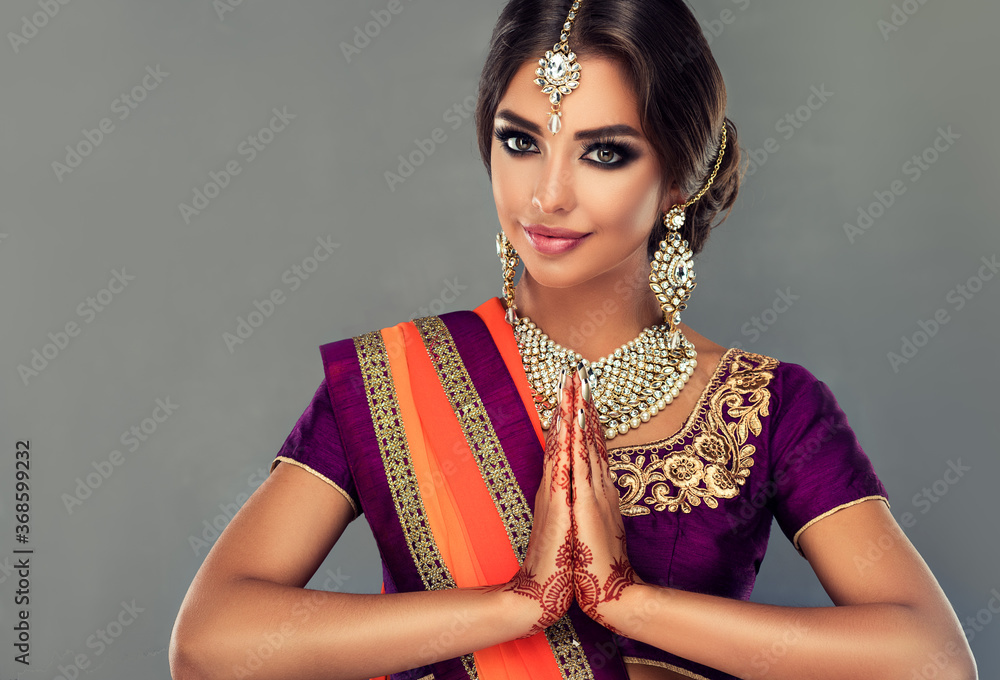 Portrait of a beautiful indian girl in a greetting pose to Namaste .India woman in traditional sari dress and jewelry. - obrazy, fototapety, plakaty 