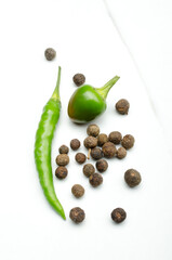 Vertical image.Closeup of fresh green chili pepper and dry black peppercorns on the white kitchen table