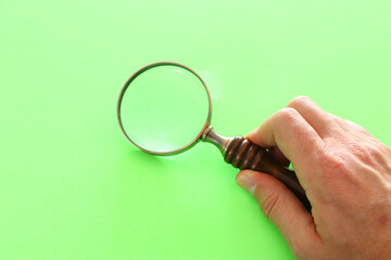 Wall Mural - vintage magnifying glass with wooden handle over green pastel background.