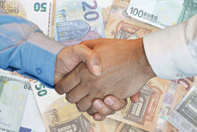 Handshake Of Two Hands Men Closeup On Background Euro Banknotes. Handshake Over Euro Money. Image Of Handshake A Trusted Business Partnership With Euro Bank Note Background.