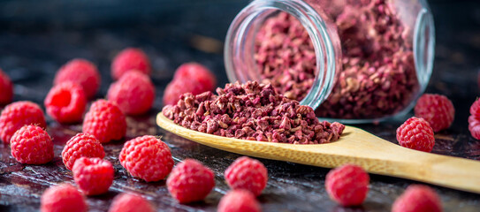 Freeze dried raspberries in a glass jar and a wooden spoon on a black background. Concept of berry storage types