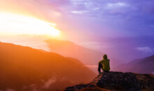 A Lonely Man Sitting On Top Of A Mountain And Watching A Beautiful And Colorful Sunset In Nepal. A Trekker Resting On Top Of A Mountain In Langtang National Park.