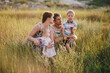© polinaloves - Happy family of young parents and their little children walking in a field at sunset.