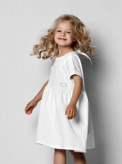 Little blonde curly positive princess girl in white casual dress and sneakers standing walking with curly hair over grey wall