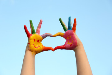kid with smiling face drawn on palms against blue sky, closeup