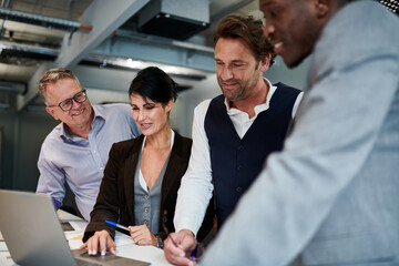 Confident mature businesswoman planning strategy with male colleagues while using laptop at office during meeting