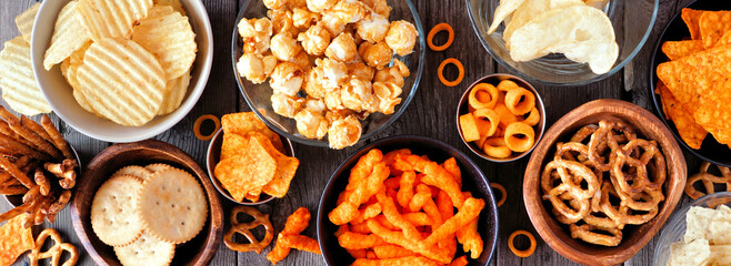 Wall Mural - Variation of salty snacks. Overhead view table scene on a dark wood banner background.