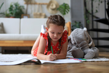 smilling happy girl lying on warm floor with a toy elephant near to her enjoying creative activity, 