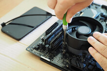 The Process Of Attaching The CPU Cooler To The Motherboard With A Green Metal Screwdriver