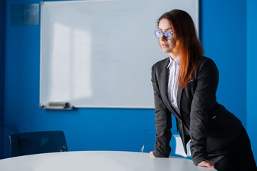 A female business coach in glasses and a suit gives a presentation in the conference room. Woman boss waiting for negotiations with partners and colleagues in the meeting room. Office employee.