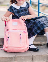  A girl in a blue school dress, white tights and shoes sits on the steps with a pink backpack