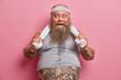 © wayhome.studio  - Portrait of fat bearded man with sweaty body, feels tired after exhausting exercises in gym, has big belly sticking out from t shirt, keeps hands on towel, does sport regularly to loose weight