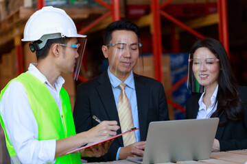 Portrait of attractive Asian businessman and investor woman, engineer, wearing protective face shield in warehouse, new normal after Covid-19 Corona virus pandemic.