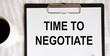© Veranika - Text Time to negotiate on the page of a notepad lying on financial charts on the office desk. Near the calculator. Business concept.