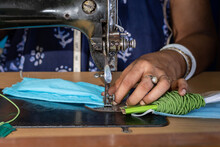 Indian woman working on old sewing machine, making homemade face masks against coronavirus or covid19 spreading, closeup detail on moving needle and fingers holding fabric	