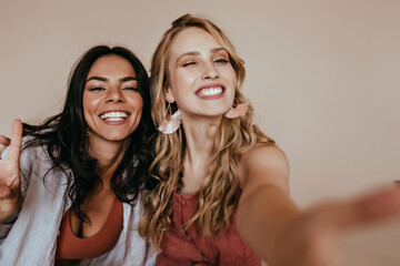 Wall Mural - Excited blonde woman with glamorous accessories making selfie. Indoor photo of ecstatic girls funny posing in studio.