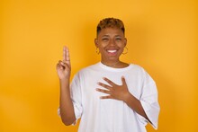 Young African American Girl With Afro Short Hair Wearing White Tshirt Standing Over Isolated Yellow Wall Smiling Swearing With Hand On Chest And Fingers Up, Making A Loyalty Promise Oath.