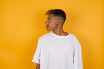 Close up side profile Young African American girl with afro short hair wearing white tshirt standing over isolated yellow wall ready to have a walk.