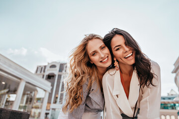 Ecstatic long-haired girls posing in spring day on sky background. Outdoor photo of two good-looking female friends.