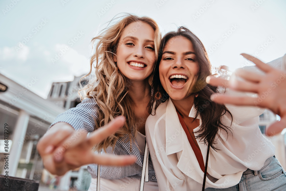 Lovable caucasian girls expressing positive emotions to camera. Outdoor photo of refined sisters posing on sky background. - obrazy, fototapety, plakaty 