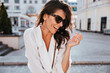 © Look! - Fascinating female model in earrings laughing in good day. Attractive brunette woman in sunglasses having fun outdoor.